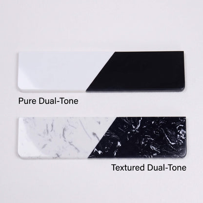 A comparison shot of two quartz stone wrist rests stacked vertically. The top one is labeled "Pure Dual-Tone" featuring solid black and white sections. The bottom one is labeled "Textured Dual-Tone" featuring black and white sections with marble patterns.